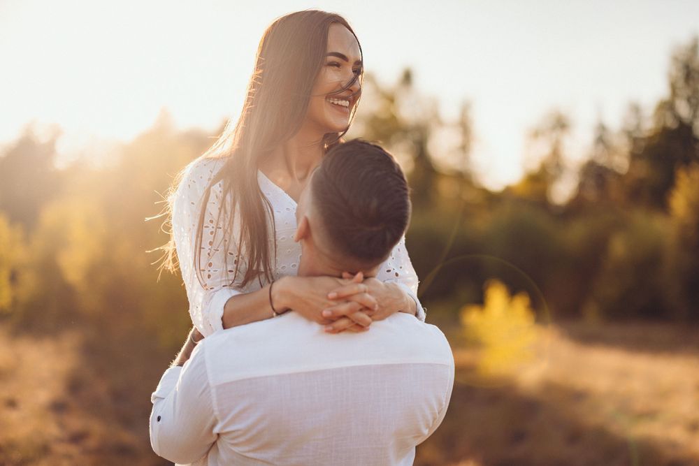 Joyful embrace in a sun-drenched field with autumn colors in the background.