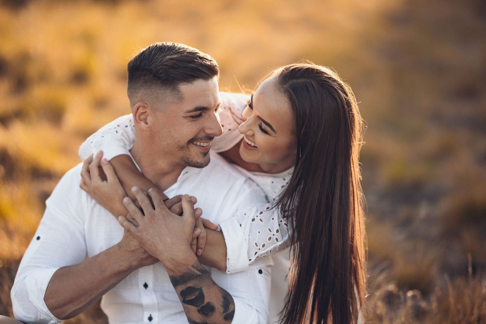 Playful couple sharing laughter against warm autumn scenery.