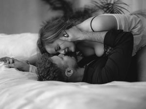 Black and white photo of two people in intimate embrace lying down on white bedding.