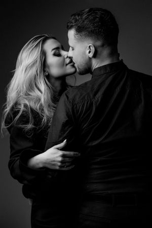 Intimate black and white portrait of a couple in dark formal attire.