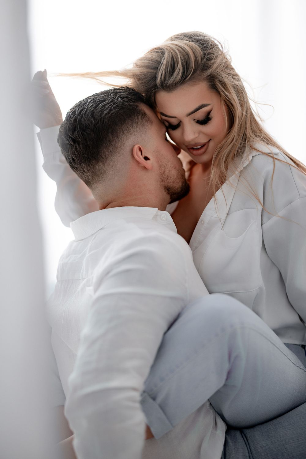 Intimate portrait of a couple in white clothing against bright background.