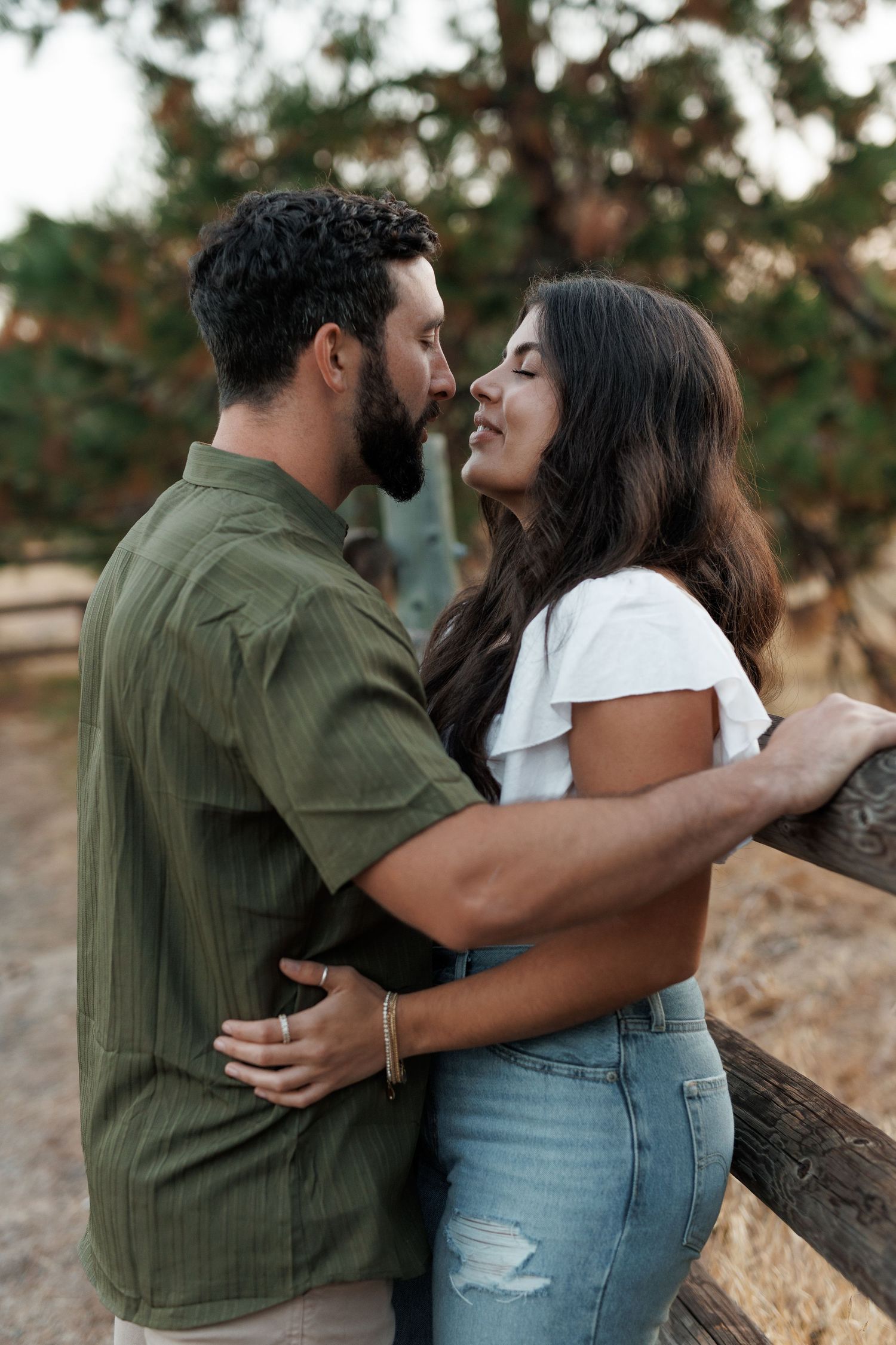 Romantic couple embraces outdoors sharing an intimate moment against a natural backdrop by a river in warm lighting.