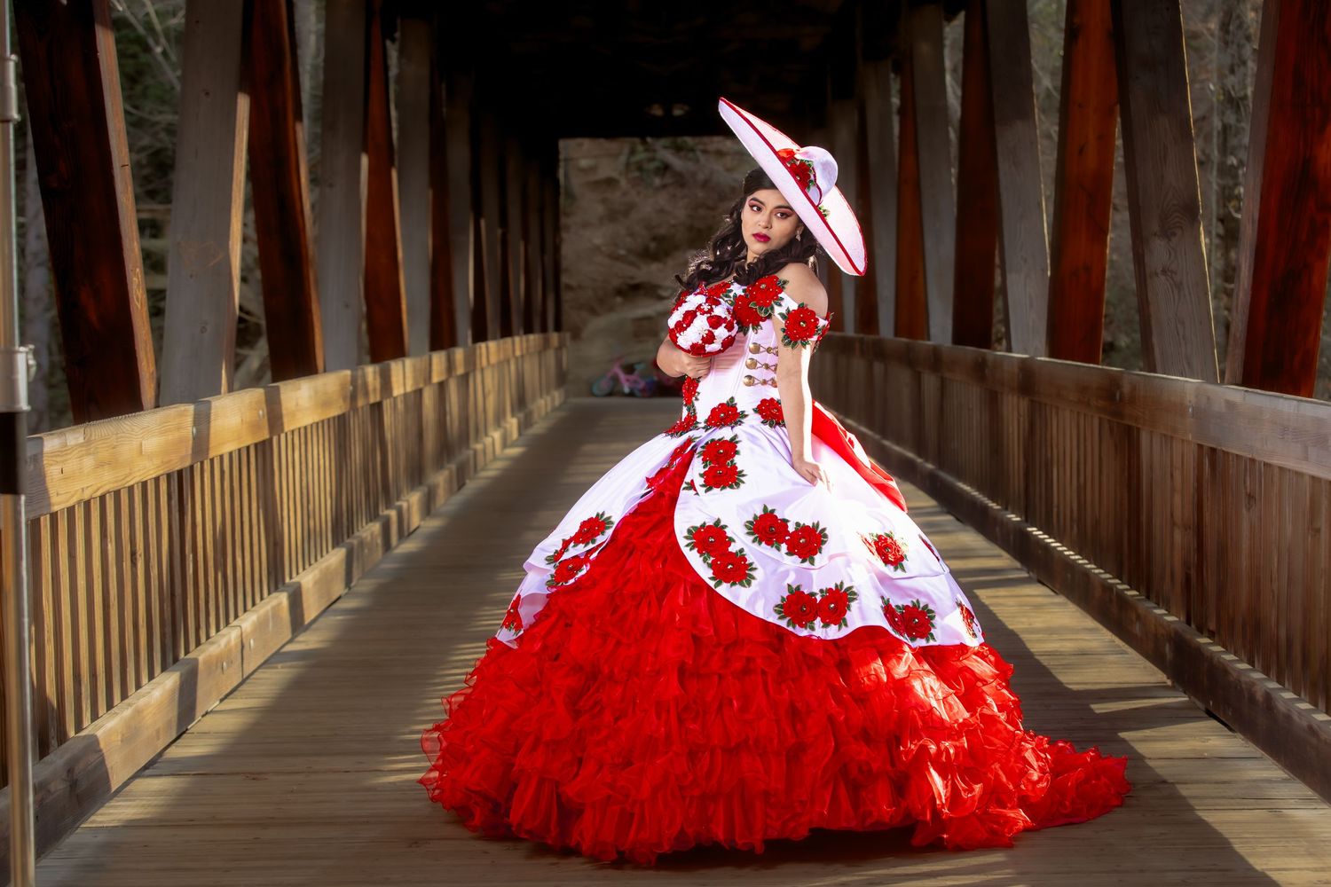 Red and white quinceañera dress photographed in sequence along a wooden bridge.