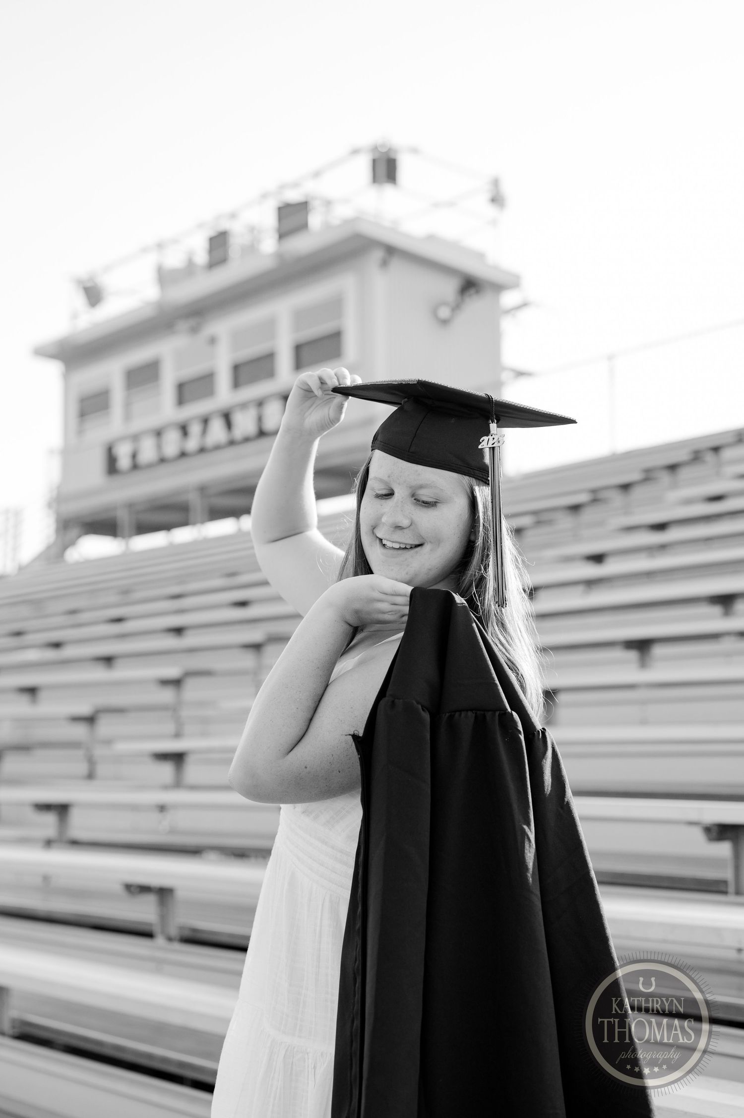 Black and white portrait of graduate in cap and gown posing on bleachers.