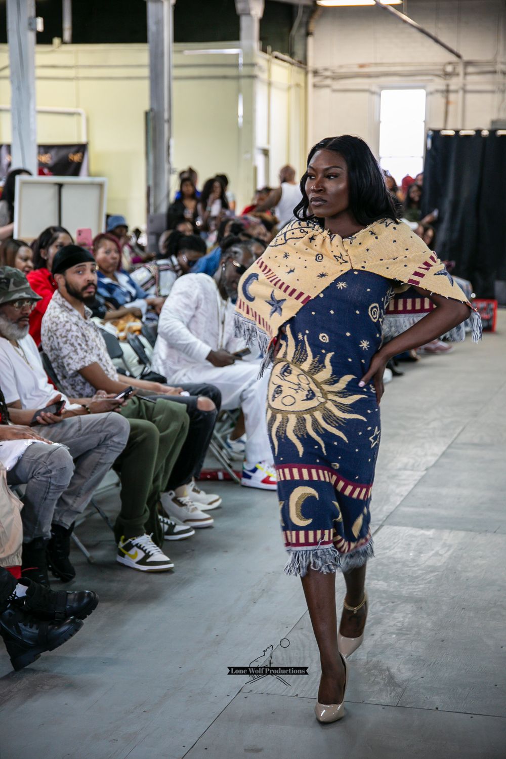 Designer celestial dress with sun and moon motifs displayed at industrial venue fashion show.