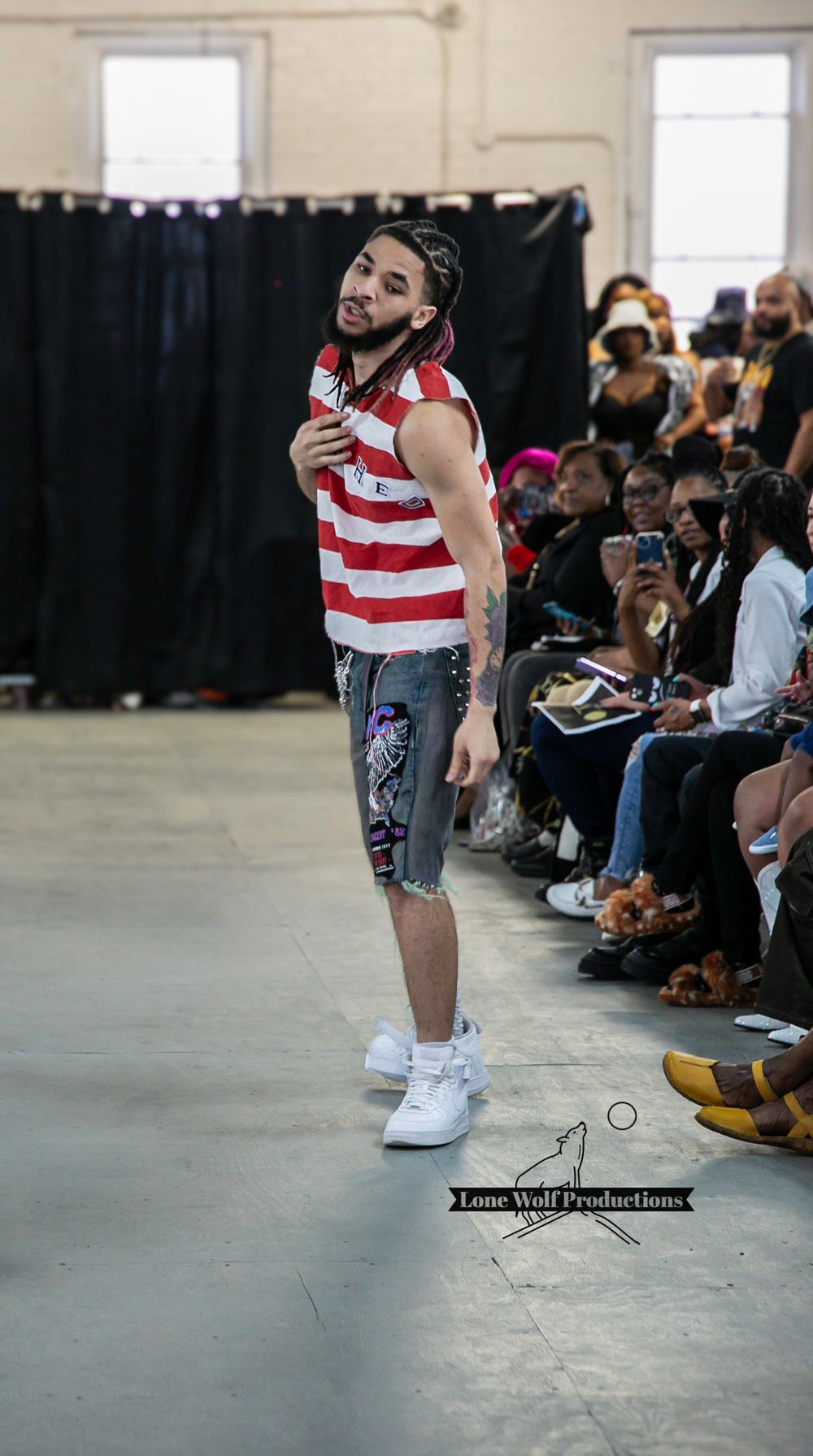 Model poses in patriotic striped tank top and printed shorts during runway presentation.
