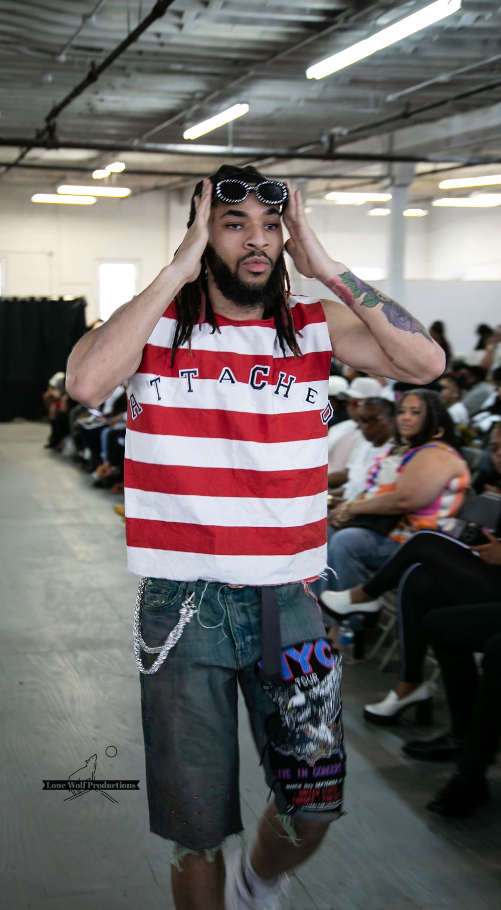 Model poses in striped top and jean shorts with sunglasses during indoor fashion show.