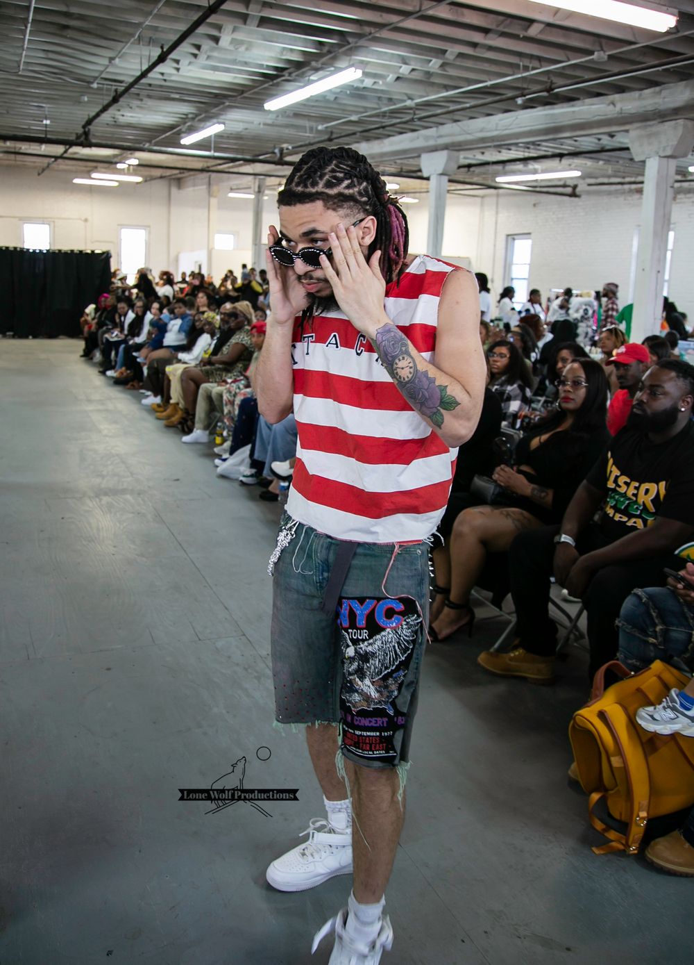 Model in casual striped outfit walks runway at fashion event with audience in background.