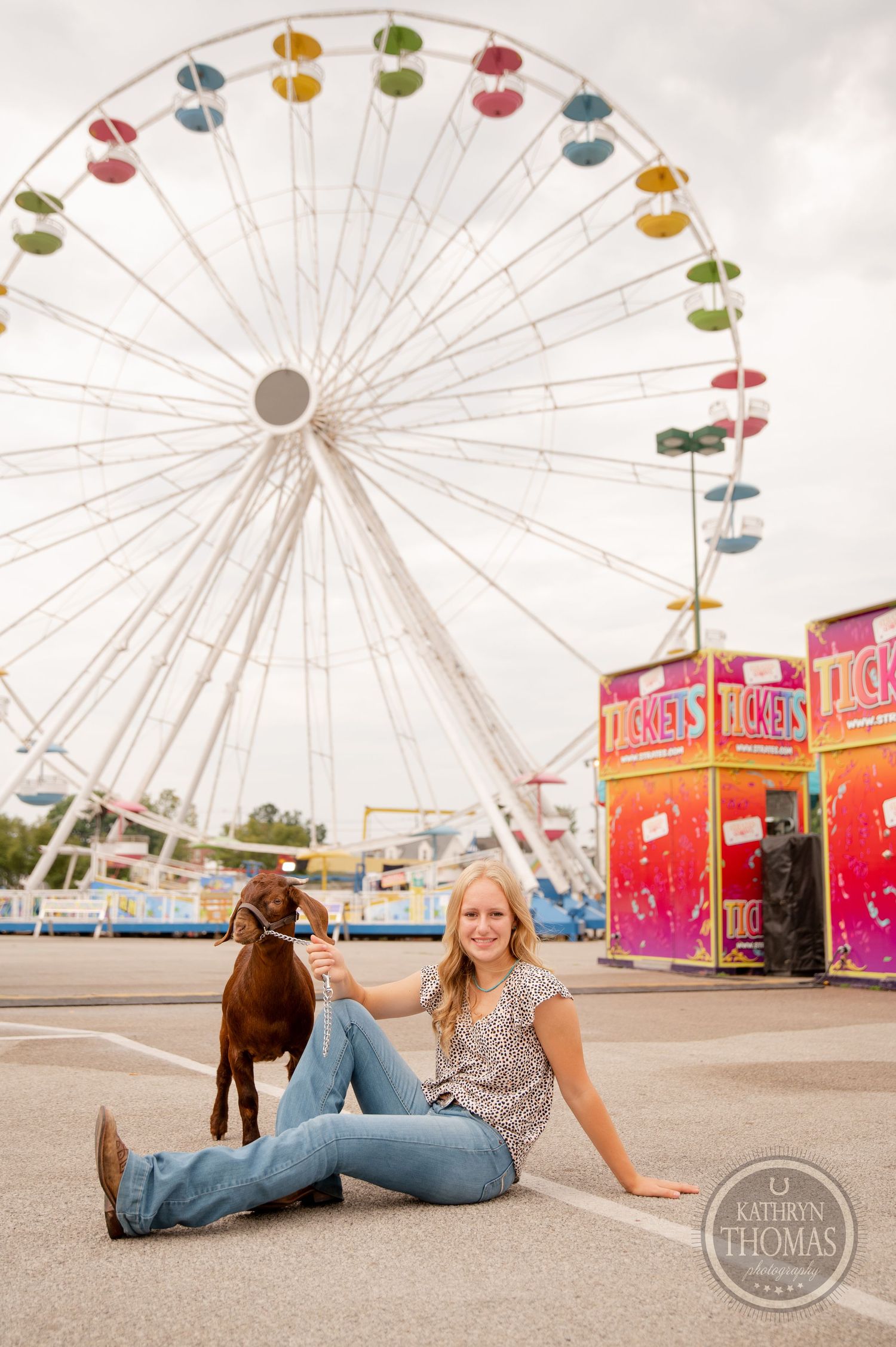 A show goat and handler relax in front of a colorful ferris wheel at a fair.