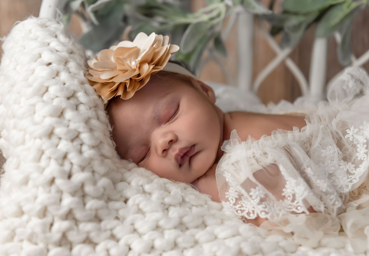 Baby wearing knit bear hat and red outfit lying on cream blanket.