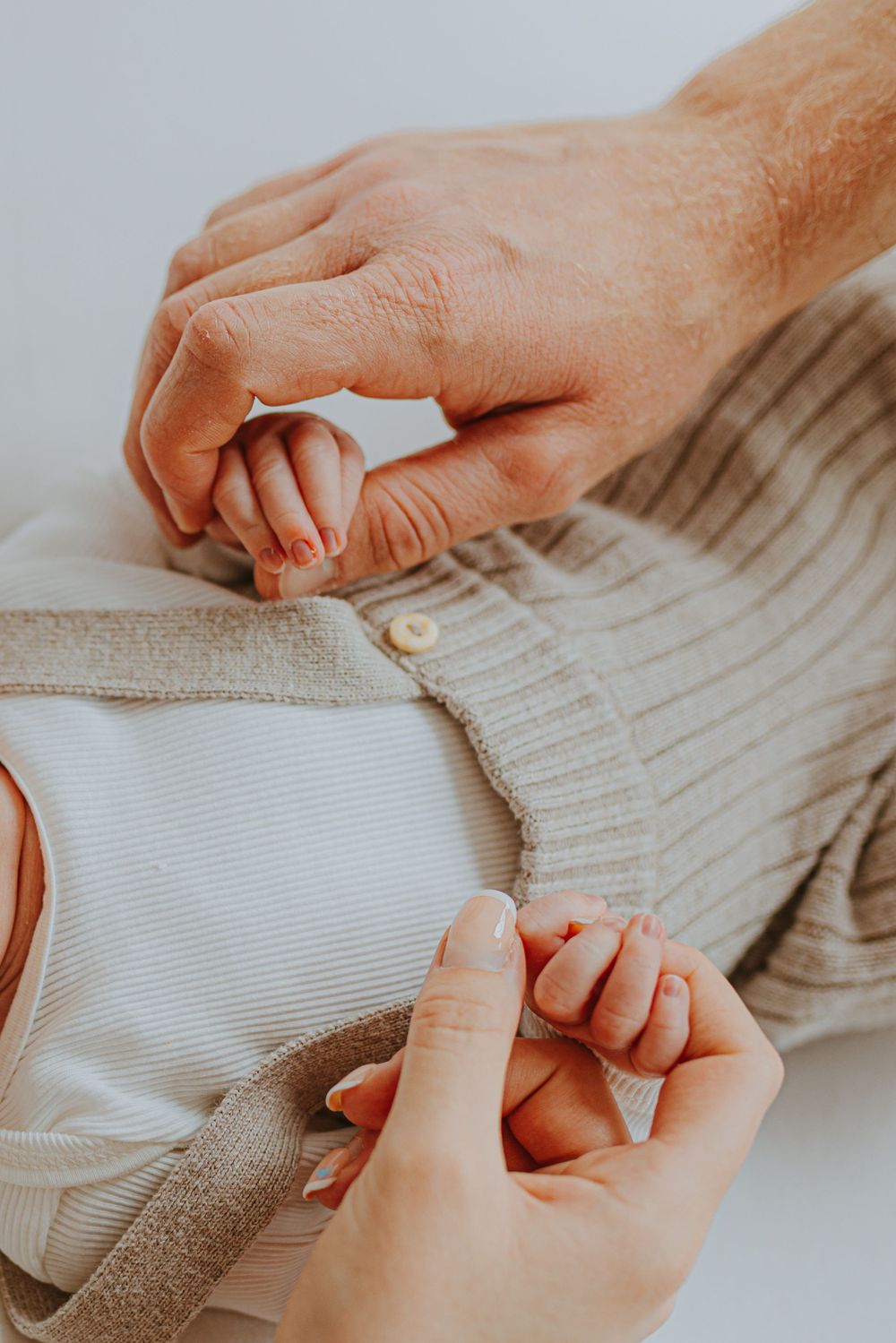 Hands gently adjusting soft knit fabric around a newborn during photo session.