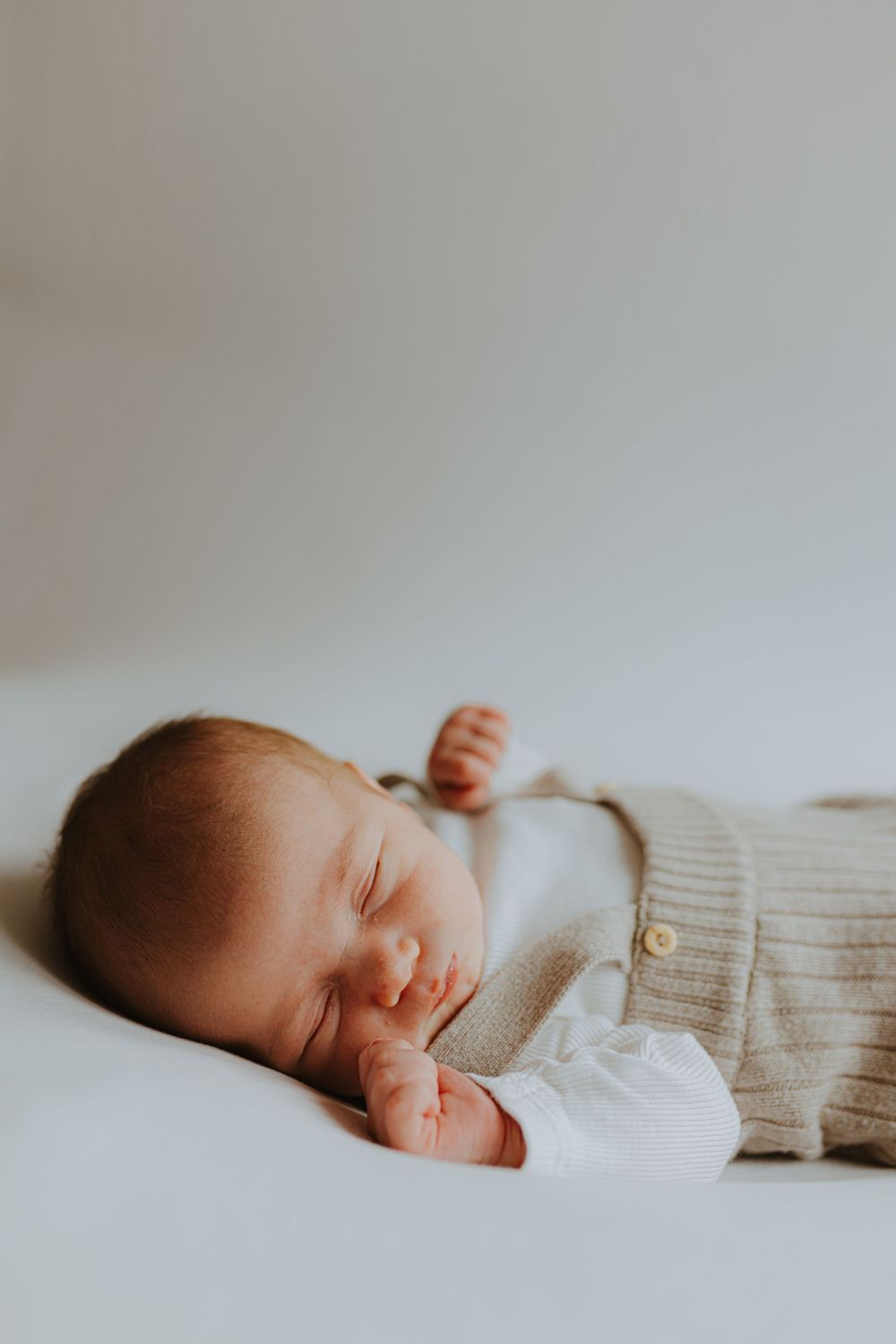 Peaceful newborn baby sleeping in cozy knit sweater against light background.