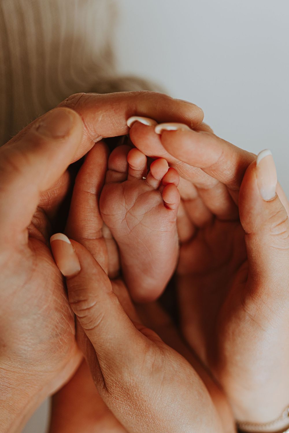 Close-up of adult hands gently holding tiny newborn fingers.