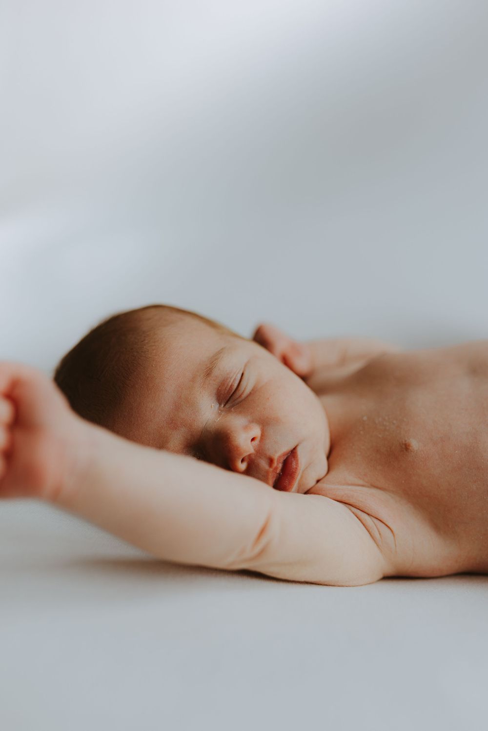 Artistic side view of sleeping newborn baby on minimalist white background.