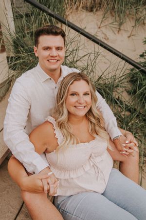 A couple sitting together on wooden steps surrounded by beach grass.