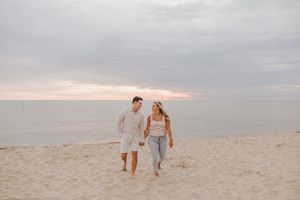 A couple walks hand in hand along a serene beach during golden hour.