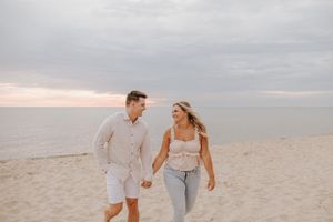 A couple strolls together on a peaceful beach with overcast skies.