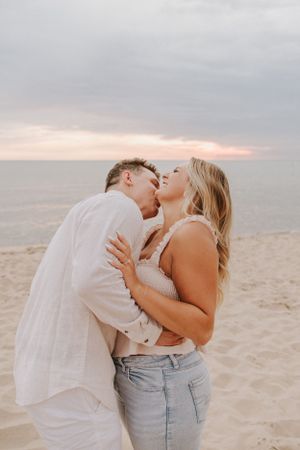 A tender moment between a couple embracing on a sandy beach during sunset.
