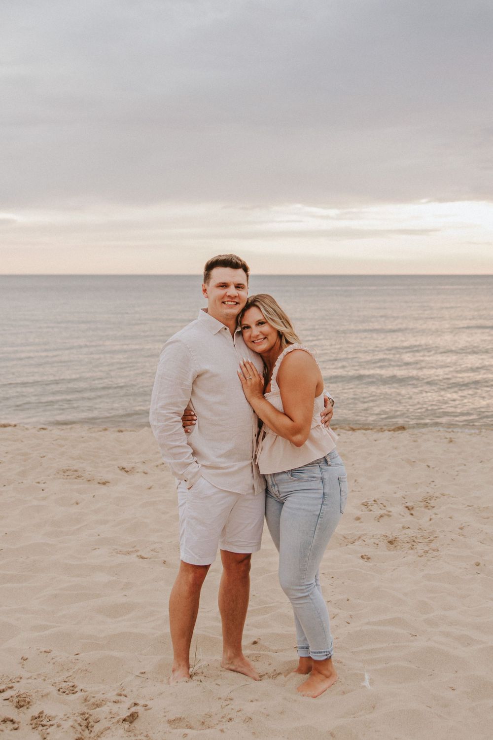 Couple in casual beach attire sharing tender moments on sandy shoreline.