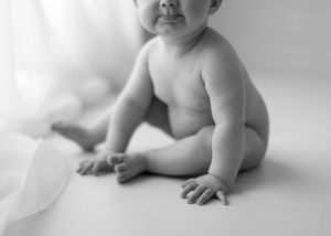 Black and white portrait of a chubby baby sitting on white background.