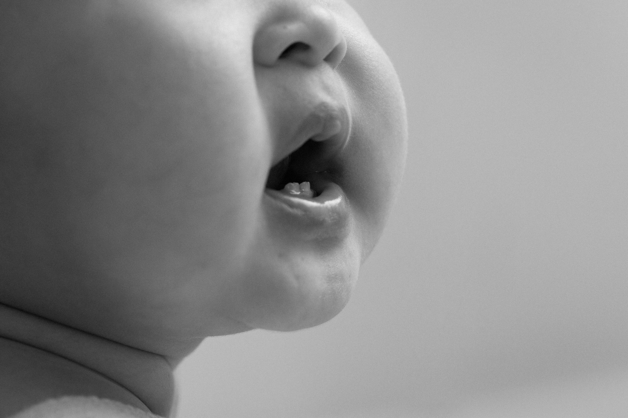 A close-up black and white photograph shows a child's open mouth in profile against a soft, blurred background.