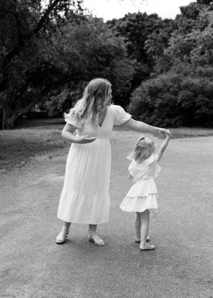Mother and daughter in white dresses dancing together on a garden path in black and white.