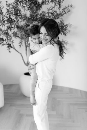A parent in white clothing holding and embracing a small child against a bright minimalist background.