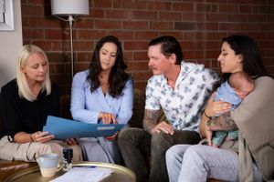 A group of people review documents together while sitting on a couch in front of a brick wall background.