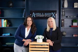 Two colleagues stand behind a wooden crate in an office with navy blue shelving.