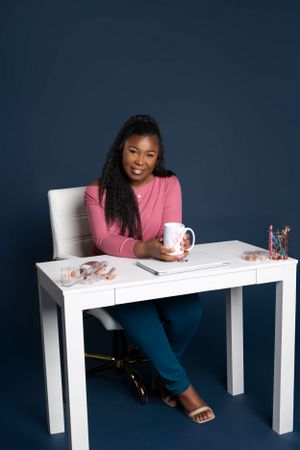 Someone in a pink sweater sits at a white desk with a coffee mug against a navy blue background.