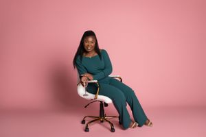 A personal branding photo teal loungewear set sits comfortably in a white office chair against a pink backdrop.