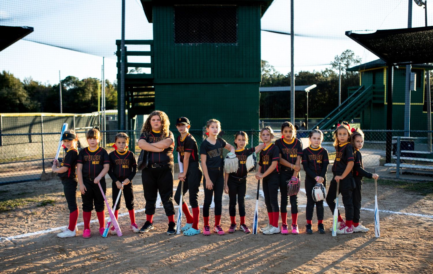 Youth softball team in red uniforms poses in formation on baseball diamond.