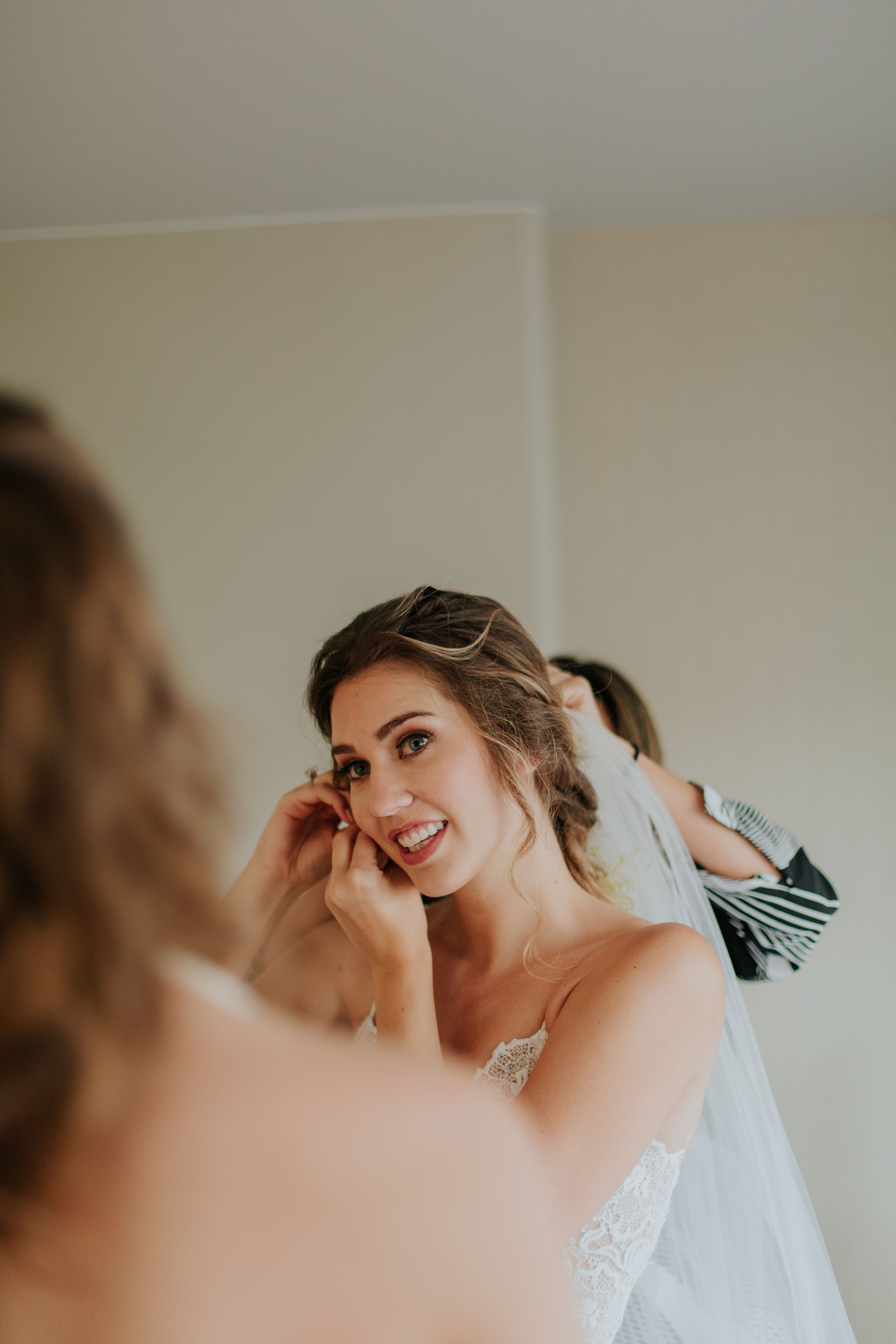 Candid getting ready moment showing joyful preparations with wedding veil and makeup.