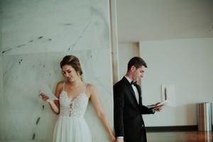 Creative first look photo with couple reading letters while standing separated by a wall.