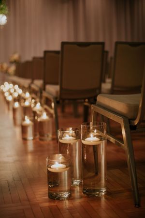 Elegant wedding ceremony aisle lined with glowing candle holders and formal chairs.