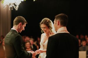Emotional exchange of rings during wedding ceremony with guests watching in background.