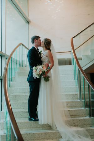 A bride and groom share an intimate moment on a modern staircase with glass railings.