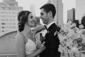 Black and white portrait of a wedding couple embracing against a city skyline backdrop.