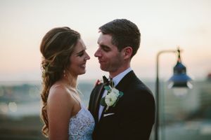 Newlyweds share a romantic moment at sunset against a blurred cityscape background.