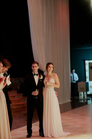 A couple celebrates during their wedding reception in front of elegant white draping and ambient lighting.