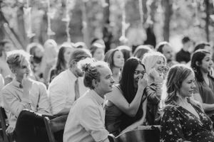 Black and white photo of wedding guests seated outdoors at a ceremony enjoying the celebration.