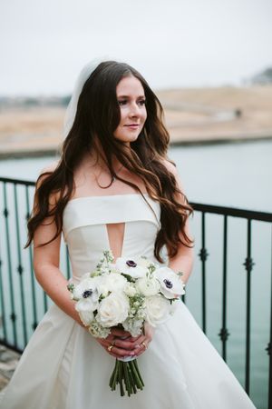 Bride in strapless ballgown holds white and blush bouquet against waterfront backdrop.
