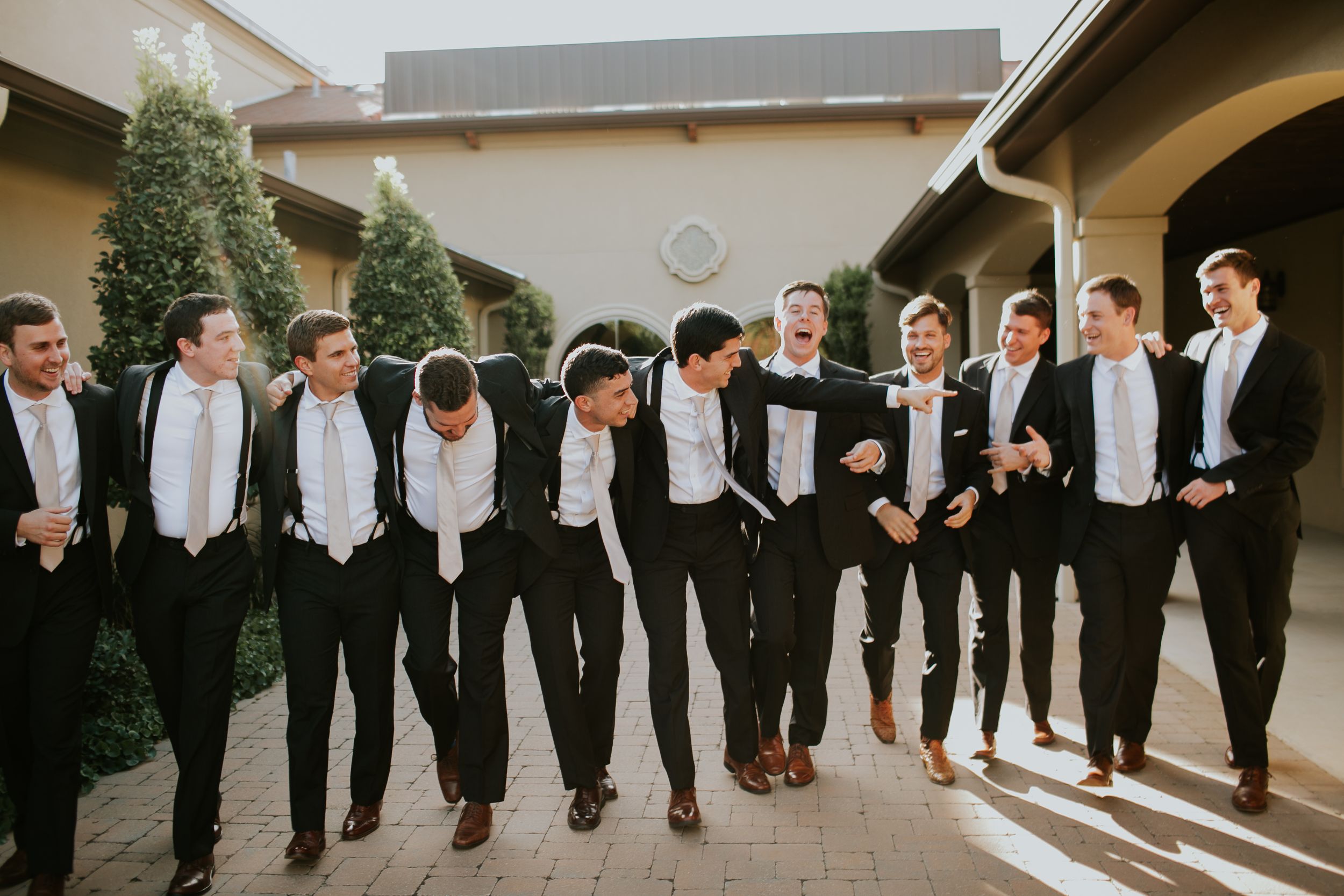 Group of groomsmen in matching tuxedos pose together outdoors.