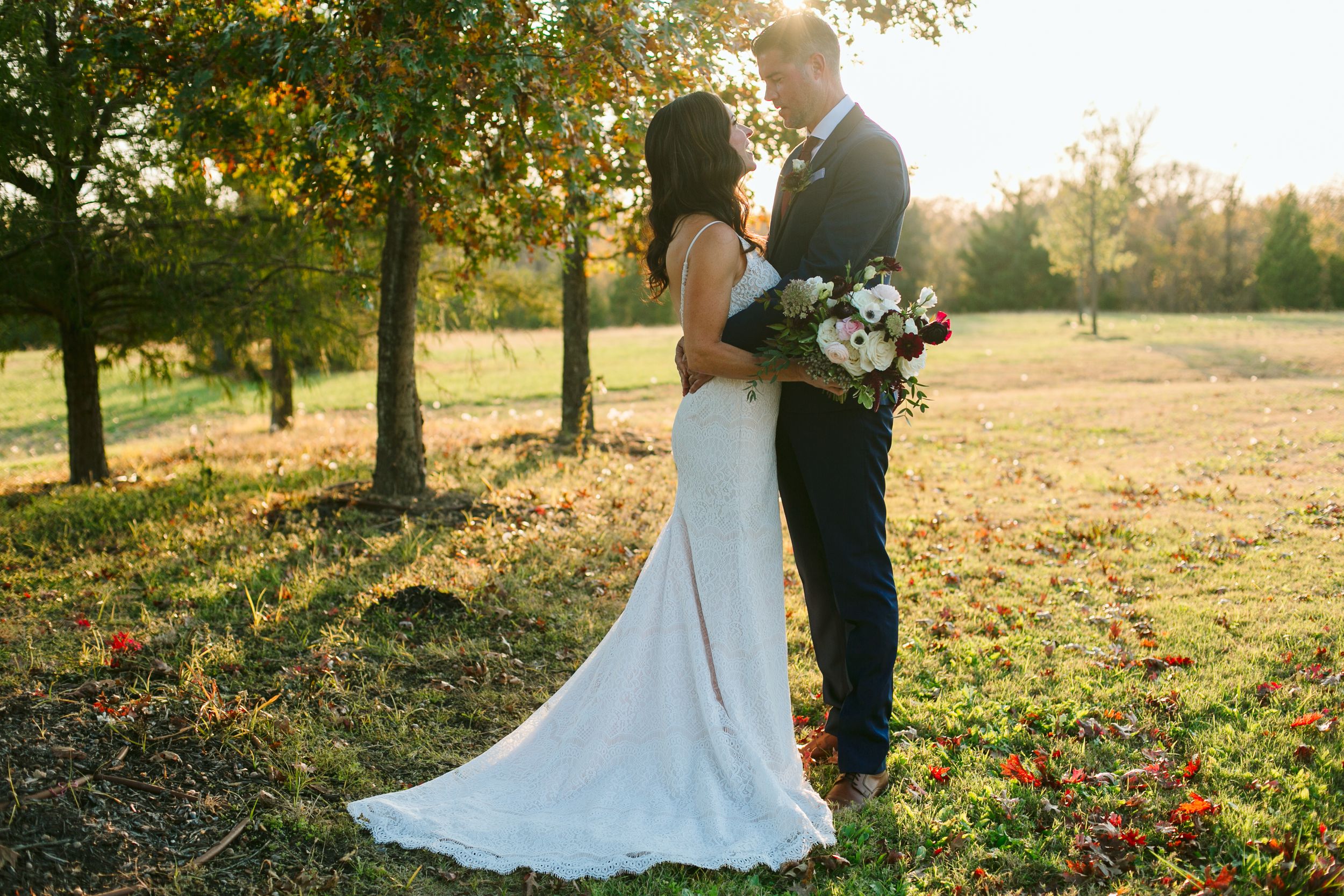 Romantic sunset portrait of couple in formal attire embracing in an autumn field.