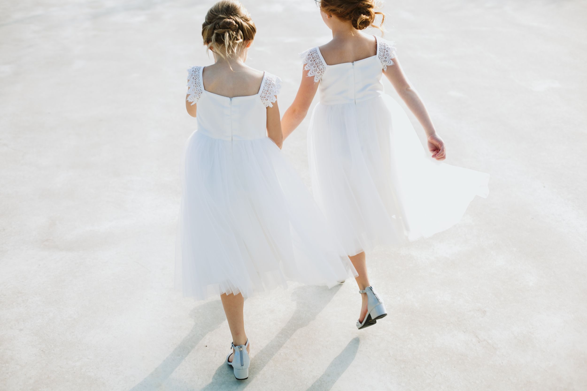 Two figures in flowing white dresses and blue sneakers run together on a bright surface.