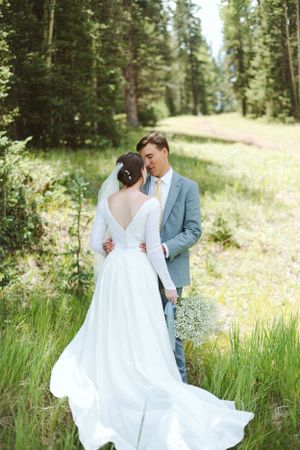 Couple sharing intimate moment in summer meadow with bride's flowing white dress.