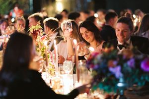 Elegant candlelit dinner party with guests raising wine glasses, surrounded by colorful floral centerpieces at a formal event.