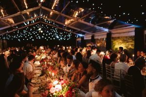 Elegant outdoor wedding reception under a twinkling light canopy with guests dining at long floral tables at night.