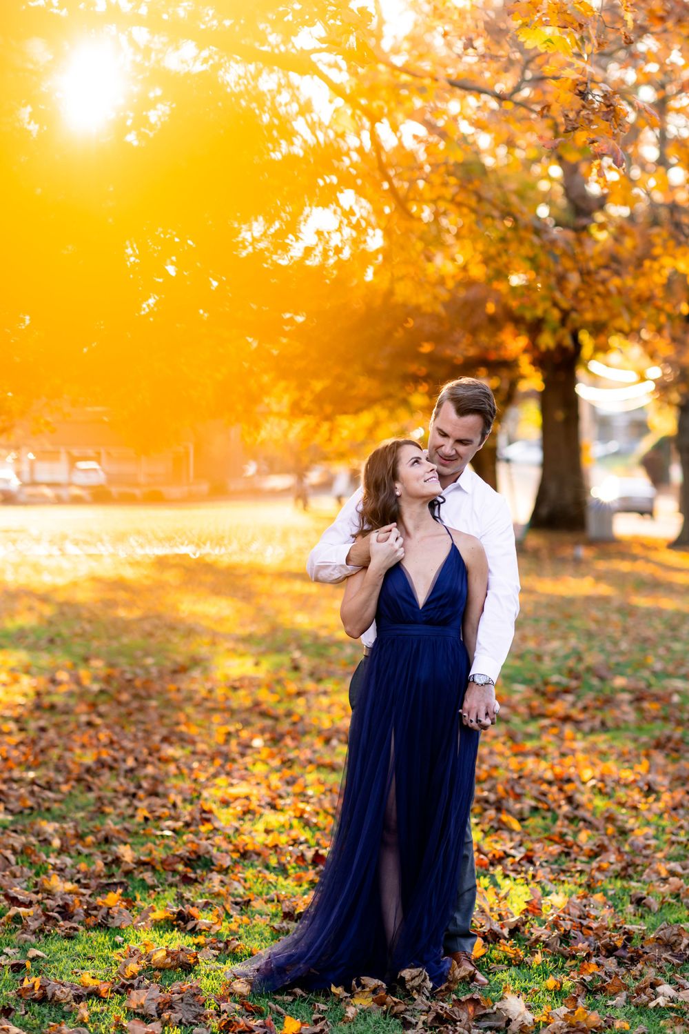 Romantic couple poses together on autumn ground covered in fallen leaves at sunset.