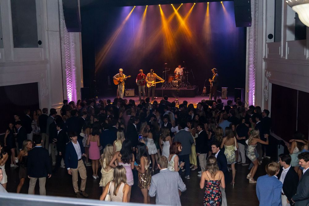 A live band performs on a lit stage while a large crowd dances at an elegant indoor venue event.